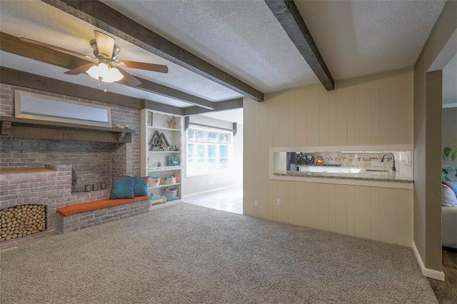 living room with beamed ceiling, a textured ceiling, a ceiling fan, carpet floors, and a fireplace