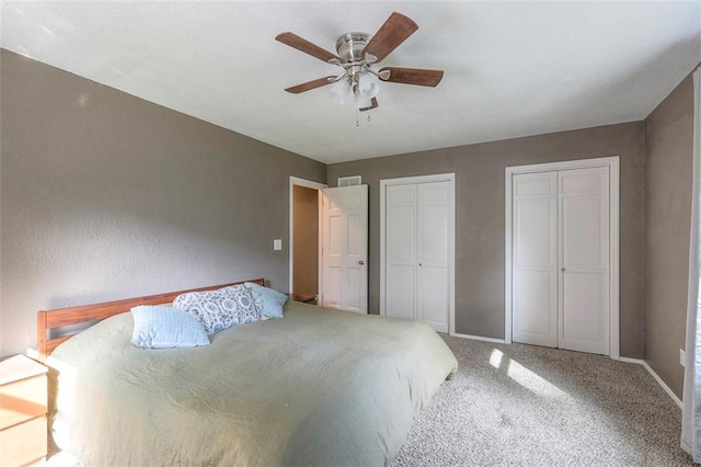 carpeted bedroom with two closets, baseboards, and a ceiling fan