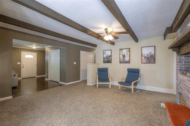 sitting room with dark carpet, beamed ceiling, baseboards, a brick fireplace, and a ceiling fan