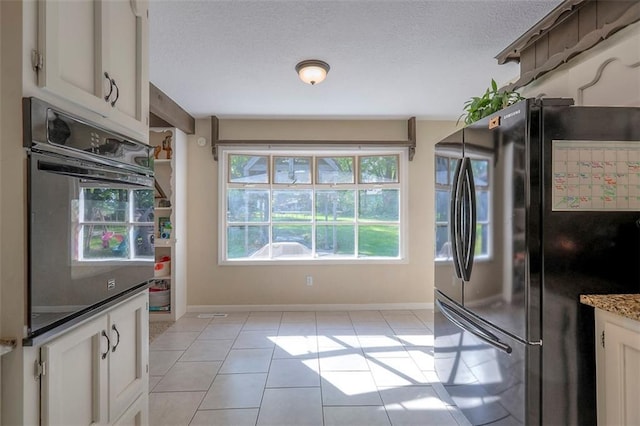 kitchen with freestanding refrigerator, oven, light tile patterned floors, white cabinetry, and a textured ceiling