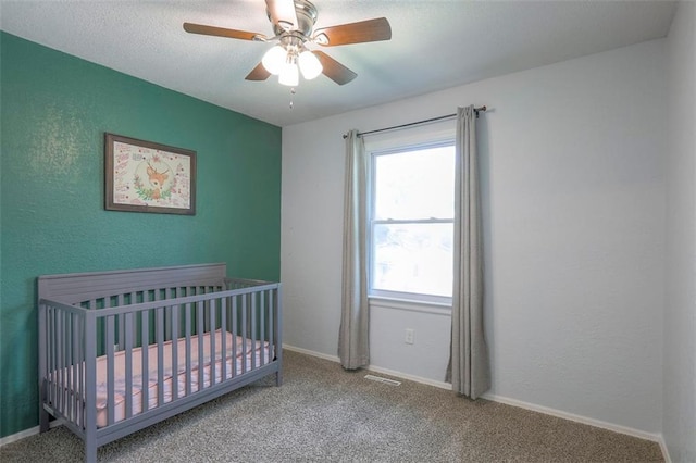 bedroom with carpet, a crib, ceiling fan, and baseboards