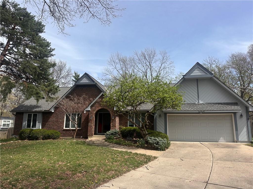 view of front of home with driveway, brick siding, an attached garage, a front lawn, and a shingled roof