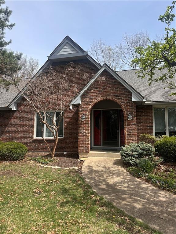 view of front of home featuring brick siding, roof with shingles, and a front lawn