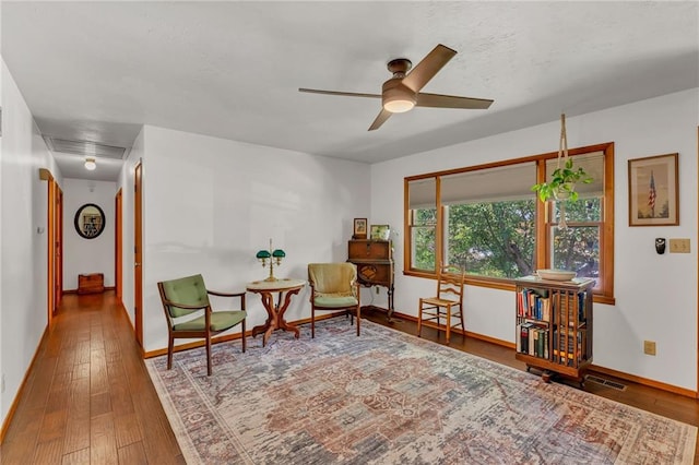 living area featuring baseboards, a ceiling fan, and wood-type flooring