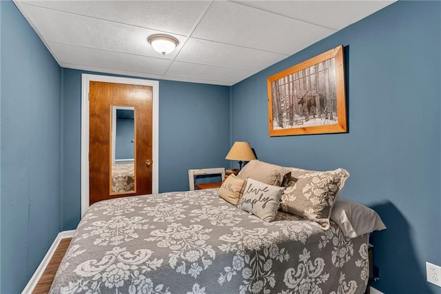 bedroom featuring wood finished floors, baseboards, and a drop ceiling