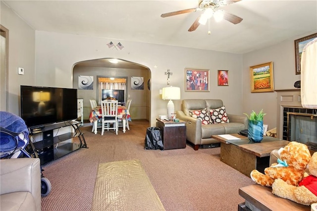 carpeted living area featuring arched walkways, a ceiling fan, and a tiled fireplace