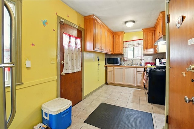kitchen with appliances with stainless steel finishes, under cabinet range hood, light tile patterned floors, a sink, and light countertops