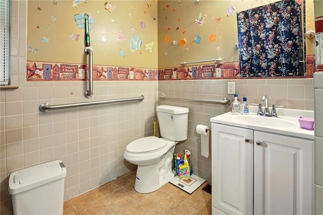 bathroom with toilet, a wainscoted wall, tile walls, vanity, and wallpapered walls