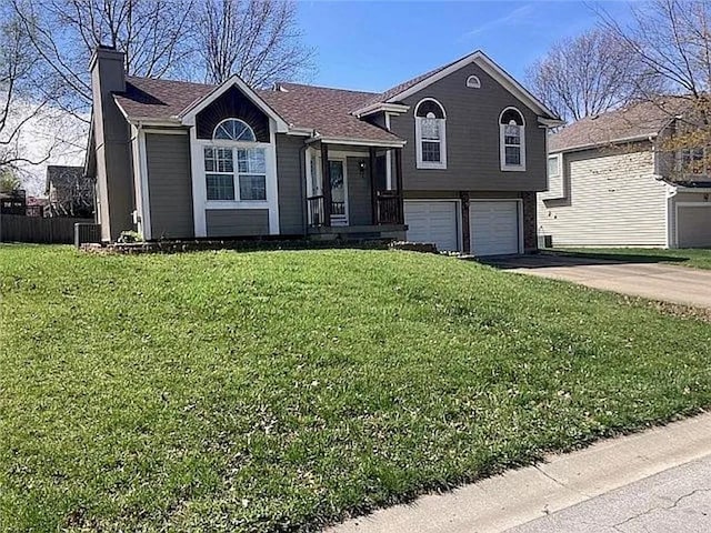split level home featuring a chimney, driveway, an attached garage, a front lawn, and cooling unit