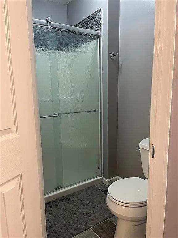 bathroom with a stall shower, toilet, and tile patterned floors