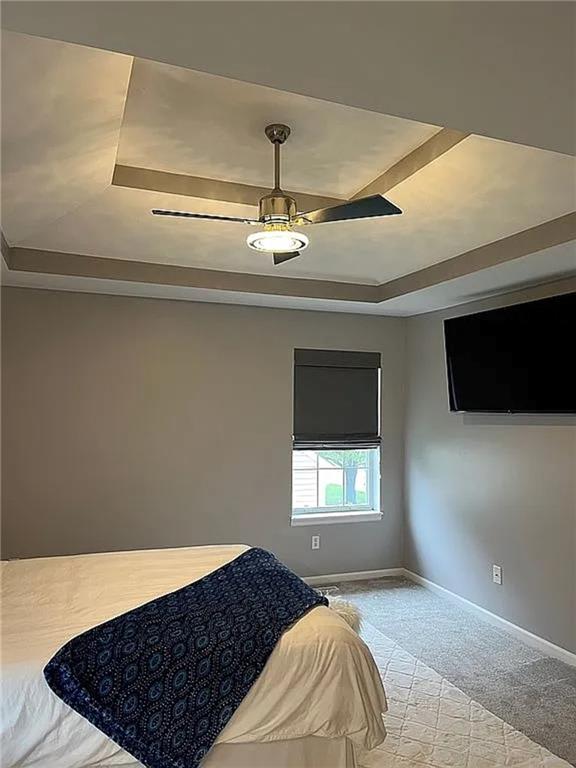 bedroom with a raised ceiling, carpet floors, baseboards, and ceiling fan