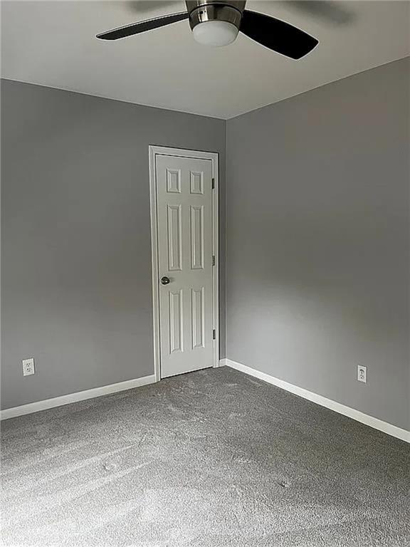 unfurnished room with ceiling fan, baseboards, and dark carpet