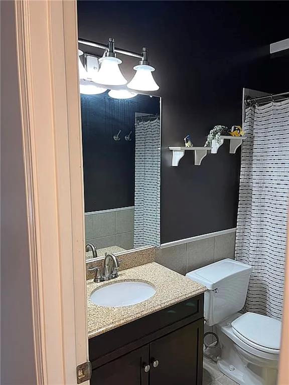 full bathroom with tile walls, toilet, vanity, tile patterned flooring, and wainscoting