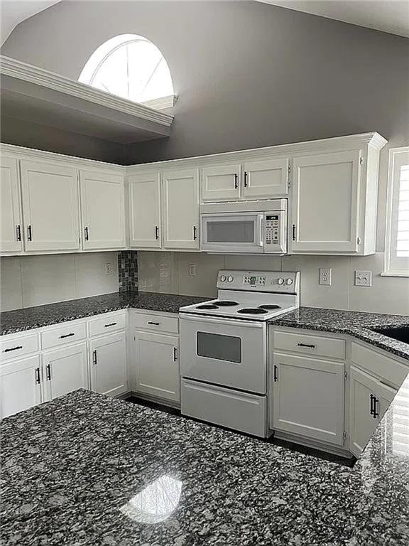 kitchen featuring white appliances, white cabinets, and dark stone counters