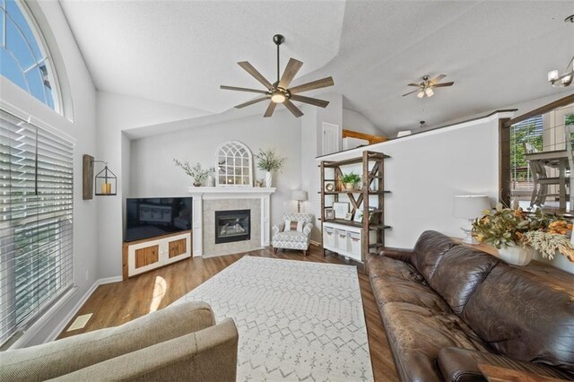 living room with a ceiling fan, lofted ceiling, a fireplace, wood finished floors, and a textured ceiling