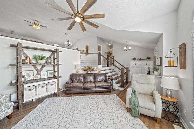 living area with vaulted ceiling, a chandelier, ceiling fan, stairway, and wood finished floors