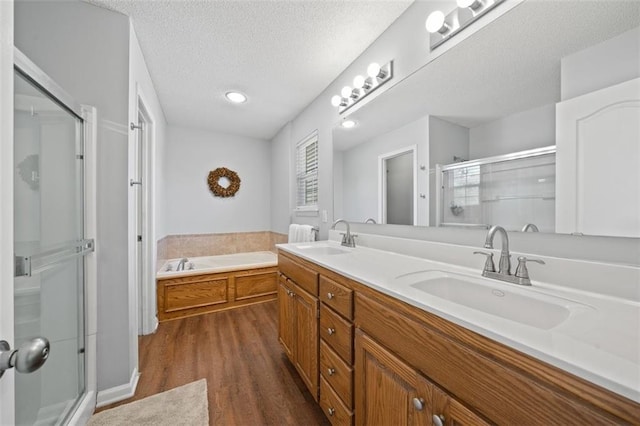 bathroom with a stall shower, wood finished floors, a textured ceiling, a bath, and double vanity