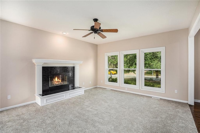 unfurnished living room with a ceiling fan, baseboards, a tile fireplace, and carpet