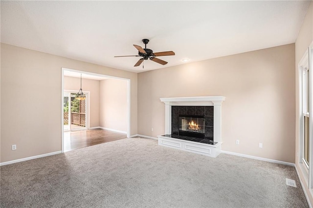 unfurnished living room featuring carpet floors, a tiled fireplace, a ceiling fan, and baseboards