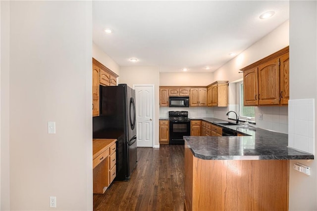 kitchen with black appliances, a sink, a peninsula, dark wood finished floors, and decorative backsplash