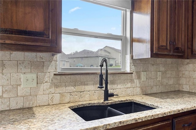 kitchen with a sink, dark brown cabinetry, light stone countertops, and decorative backsplash