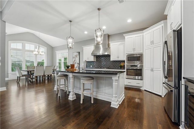 16609 Cody St, Overland Park, KS 66221 - kitchen featuring appliances with stainless steel finishes, wall chimney range hood, dark countertops, a chandelier, and a kitchen bar