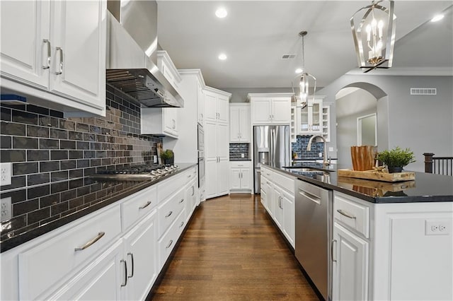 16609 Cody St, Overland Park, KS 66221 - kitchen featuring wall chimney exhaust hood, appliances with stainless steel finishes, decorative backsplash, an island with sink, and arched walkways