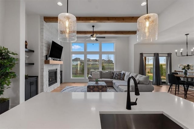 16521 S Stagecoach St, Olathe, KS 66062 - living room featuring a large fireplace, light wood-type flooring, a ceiling fan, beamed ceiling, and a chandelier