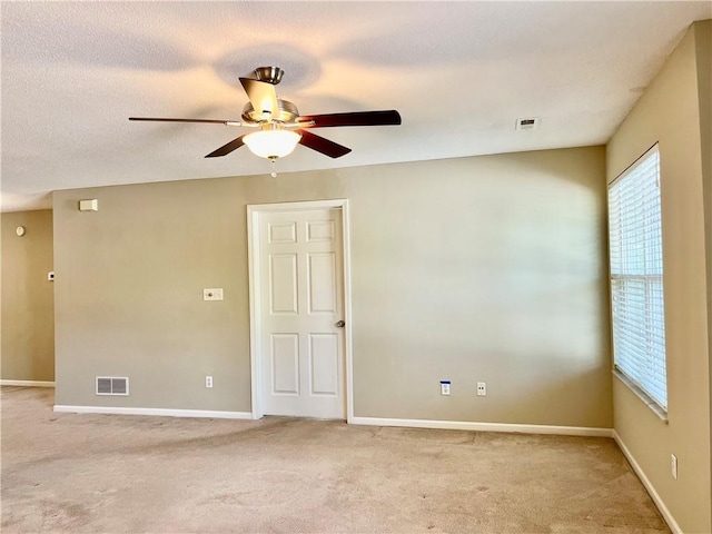 spare room with healthy amount of natural light, a ceiling fan, and light colored carpet