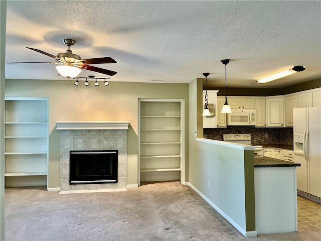 kitchen with white appliances, dark countertops, a peninsula, decorative light fixtures, and a fireplace