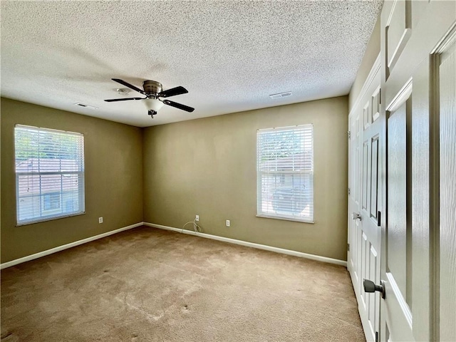 carpeted spare room with healthy amount of natural light, a ceiling fan, baseboards, and a textured ceiling