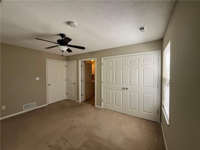 unfurnished bedroom with two closets, carpet flooring, baseboards, a textured ceiling, and a ceiling fan