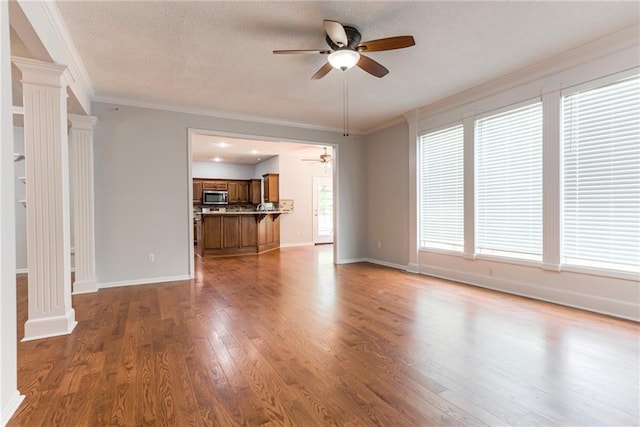 6402 W 147th Ter, Overland Park, KS 66223 - unfurnished living room with ceiling fan, wood finished floors, ornamental molding, decorative columns, and a textured ceiling