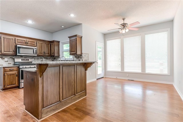 6402 W 147th Ter, Overland Park, KS 66223 - kitchen with appliances with stainless steel finishes, a breakfast bar area, backsplash, light wood finished floors, and a textured ceiling