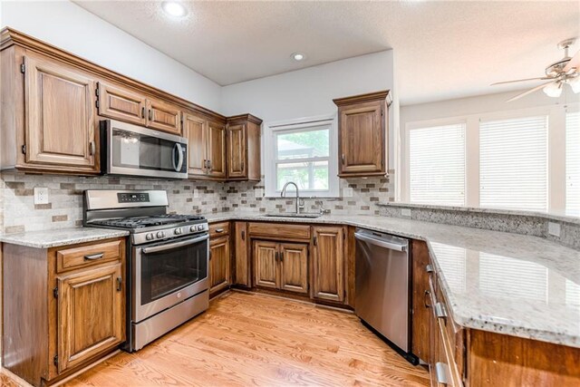 6402 W 147th Ter, Overland Park, KS 66223 - kitchen with stainless steel appliances, a sink, light stone counters, a ceiling fan, and light wood-type flooring