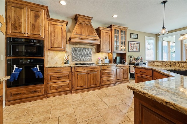 kitchen featuring custom range hood, brown cabinetry, stainless steel gas cooktop, light stone countertops, and recessed lighting