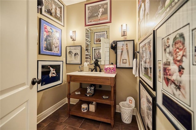 corridor featuring dark tile patterned floors, baseboards, and a sink