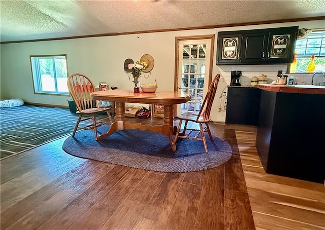 dining area featuring crown molding, a textured ceiling, dark wood finished floors, and bar with sink