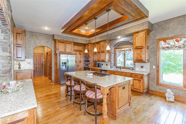 26650 W 100th Pl, Olathe, KS 66061 - kitchen featuring stainless steel appliances, arched walkways, a tray ceiling, light wood-type flooring, and light stone countertops