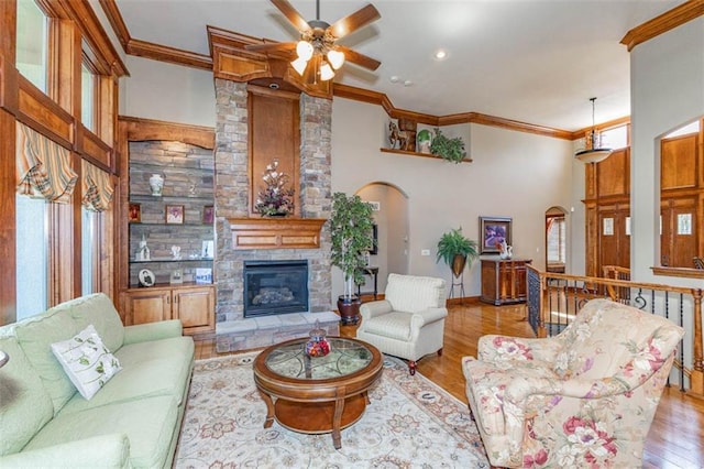 26650 W 100th Pl, Olathe, KS 66061 - living room with crown molding, wood finished floors, ceiling fan, a stone fireplace, and arched walkways