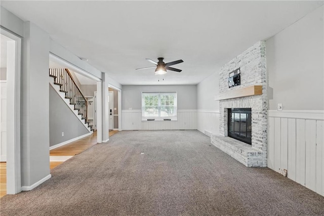 15642 W 146th Ter, Olathe, KS 66062 - unfurnished living room featuring carpet flooring, ceiling fan, a wainscoted wall, stairway, and a fireplace