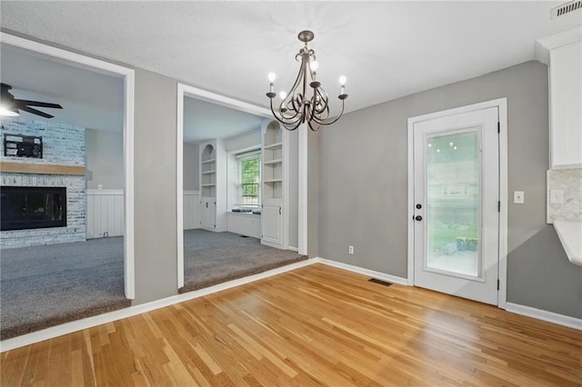 15642 W 146th Ter, Olathe, KS 66062 - unfurnished dining area with a chandelier, light wood-style flooring, a ceiling fan, a fireplace, and built in shelves