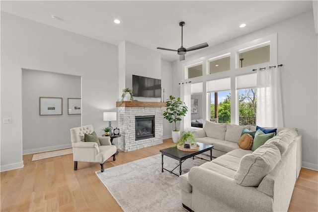 11573 S Mize Rd, Olathe, KS 66061 - living room with baseboards, a stone fireplace, a towering ceiling, a ceiling fan, and light wood-style flooring