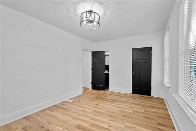 527 Cypress Ave, Kansas City, MO 64124 - spare room with light wood finished floors, a chandelier, a textured ceiling, baseboards, and a textured wall
