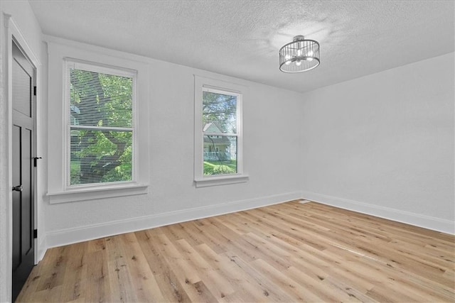 527 Cypress Ave, Kansas City, MO 64124 - unfurnished room featuring light wood finished floors, a textured ceiling, baseboards, and a chandelier