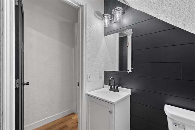 527 Cypress Ave, Kansas City, MO 64124 - bathroom with vanity, toilet, wood finished floors, a textured wall, and baseboards