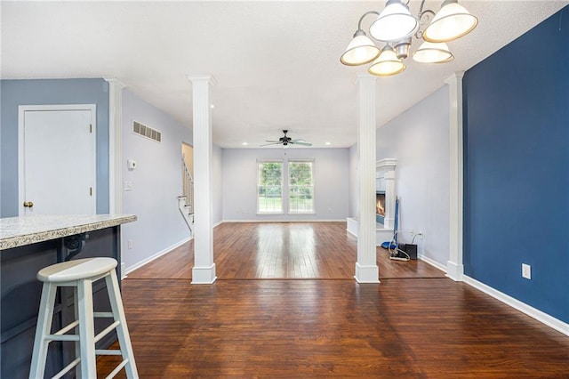 417 N Locust St, Gardner, KS 66030 - unfurnished living room featuring ceiling fan, dark wood-style flooring, decorative columns, a chandelier, and a warm lit fireplace