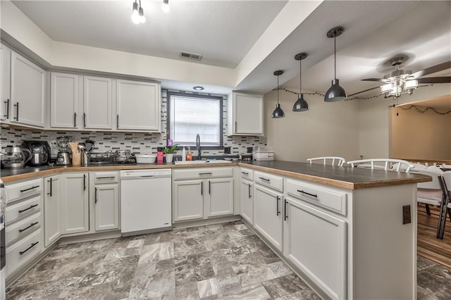 kitchen with white dishwasher, a sink, a peninsula, tasteful backsplash, and a ceiling fan