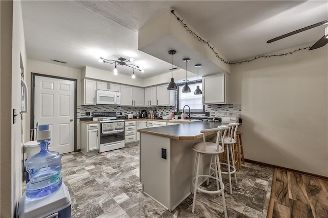 kitchen with range with electric cooktop, white microwave, a peninsula, a sink, and tasteful backsplash