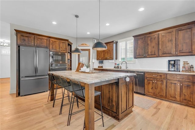 301 Sunrise Dr, Louisburg, KS 66053 - kitchen with appliances with stainless steel finishes, light wood finished floors, backsplash, a breakfast bar area, and a center island